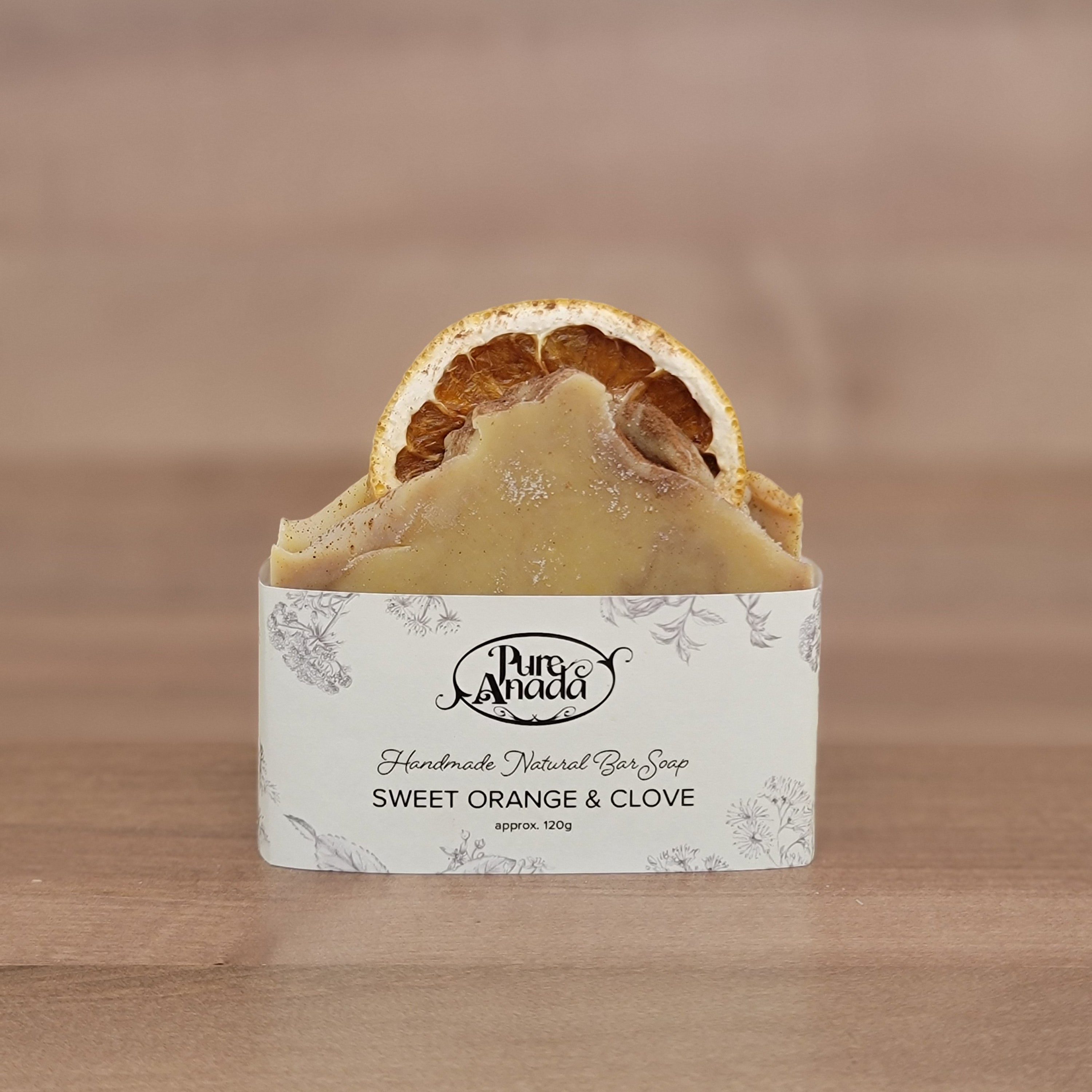 Bar of handmade Sweet orange & clove soap with a visible brand label on a wooden background